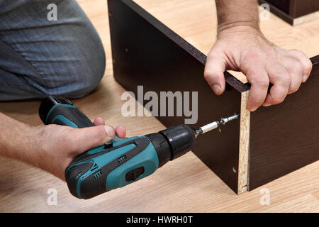 Assembling furniture from chipboard, Woodworker  screwing Chipboard screws using a cordless screwdriver. Stock Photo