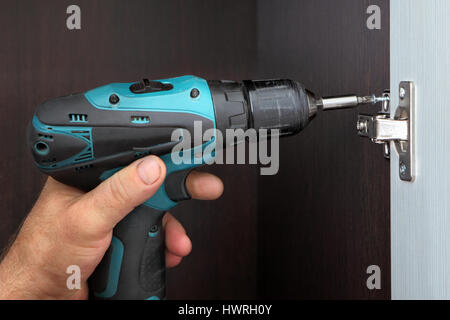 Carpenter installs door wardrobes, screw the door hinge cordless screwdriver. Stock Photo