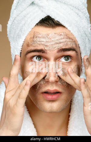 Handsome man cleans face scrub on skin. Close up of young man wearing towel on his head. Grooming himself Stock Photo