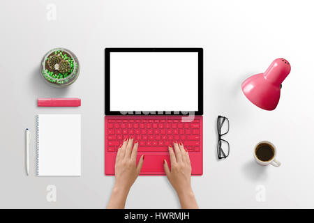 Modern tablet laptop on desk. Woman typing on keyboard. Isolated white screen for mockup. Pad, plant, glasses, coffee, lamp beside. Top view. Stock Photo