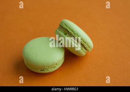 Pair of Green pistachio macaroons over orange background, horizontal view with copy space Stock Photo