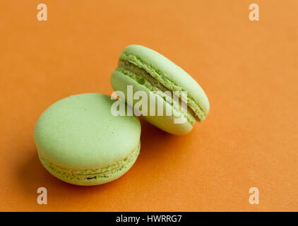 Pair of Green pistachio macaroons over orange background, horizontal view with copy space Stock Photo