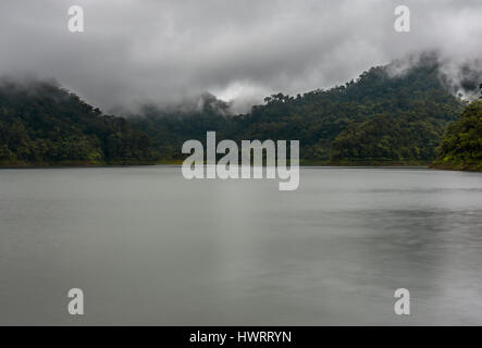 Low clouds ride over the tops of the tree covered hills at a large lake setting. Stock Photo