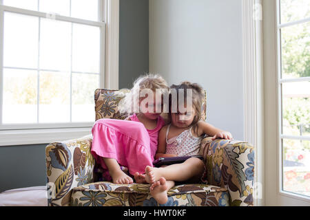 Sisters using tablet computer while sitting on armchair at home Stock Photo