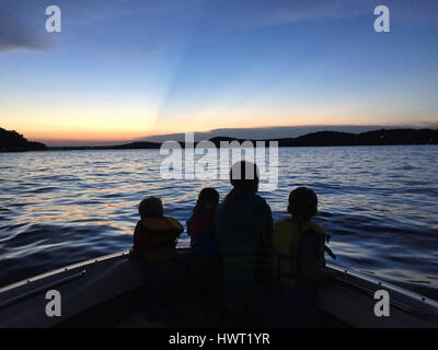 Silhouette siblings traveling in boat on Kentucky lake against blue sky during sunset Stock Photo