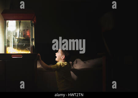 Surprised boy looking at popcorn maker in darkroom Stock Photo