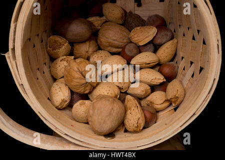 mixed nuts in basket spilling out on black table top Stock Photo
