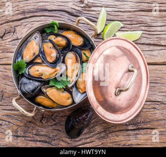 Boiled mussels in copper pan on the wooden table.