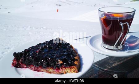 Slice of blueberry cake, mulled wine in a glass, served alfresco on skiing slope in French Alps Stock Photo