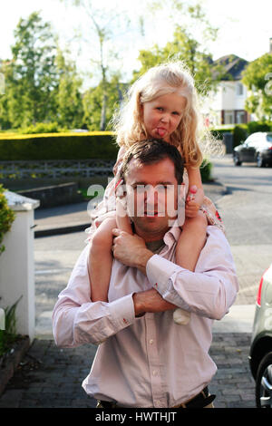 Child sticking her tongue out on Daddy's shoulders father daughter concept Stock Photo