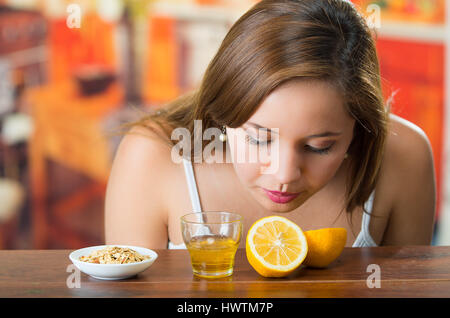 Young brunette bending over table smelling sliced lemon, glass of honey and some granola on the side