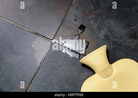 Hot water bottle lying on a bathroom floor, with some water spillage. Stock Photo