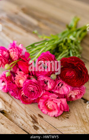 Bouquet of several pink and one dark red ranunculus lying on wooden rustic tabletop portrait layout Stock Photo