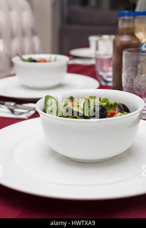 Green Salad with Lettuce, Tomato, Avocado and Olives served in White Dinnerware and Red Table Cloth Stock Photo