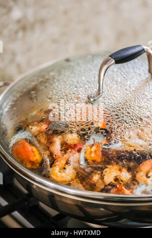 A close up view of steaming Spanish seafood paelle in a big saucepan sitting on a stove in a kitchen.  Natural light. Vertical image Stock Photo