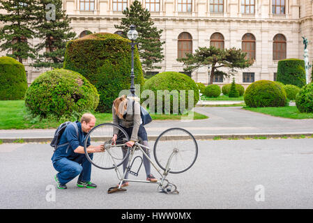 Helping hand, view of a young man and woman working together to repair a bike in Maria Theresienplatz, Vienna, Austria. Stock Photo