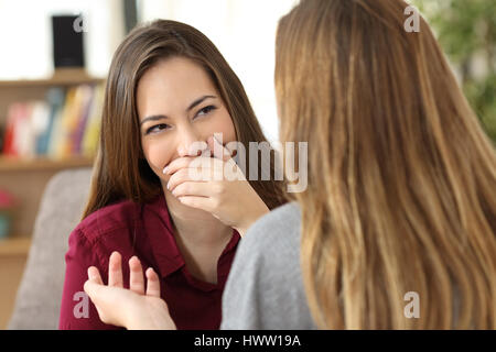 Ashamed woman hiding her smile in a conversation with a friend sitting on a couch at home Stock Photo