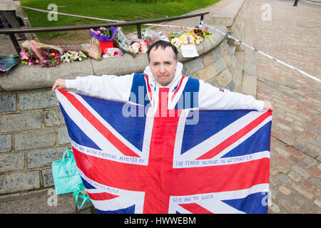 Westminster, London, UK. 23rd Mar, 2017. With his flag and a bunch of roses, John Loughrey of Streatham mourns those killed and injured in Tuesday's terrorist attack on Westminster Bridge and in the grounds of Parliament, in which three people and their attacker were killed with over 40 injured. Credit: Paul Davey/Alamy Live News