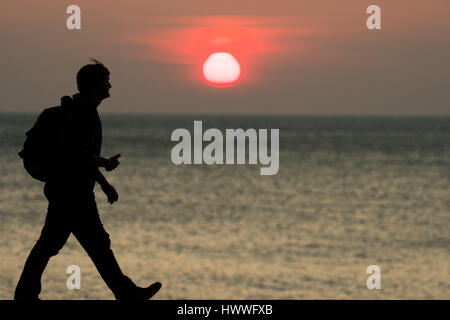 Aberystwyth Wales UK, Thursday 23 March 2017 UK Weather: A man walks along the promande in front of the spectacular sunset over Cardigan Bay in Aberystwyth on the west Wales coast Photo Credit: Keith Morris/Alamy Live News Stock Photo