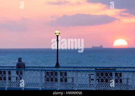 A person taking in both an early morning walk along Llandudno Pier and the sunrise as it breaks on the horizon at Llandudno, Wales Stock Photo