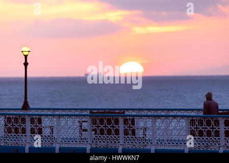 Llandudno, Wales, UK 24th March 2017, As a high breaks over parts of the UK today and through the weekend some parts including the coastal town of Llandudno on the North Wales coast will enjoy warm pleasant weather with temperatures in the mid-teens. A man enjoying an early morning walk on Llandudno Pier as the sun and a ship break the horizon © DGDImages/Alamy Live News Stock Photo