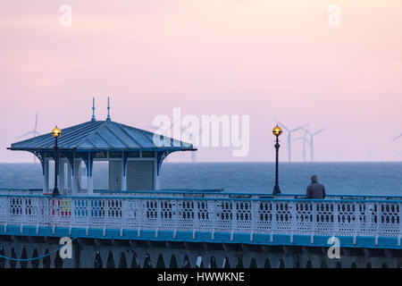 A person taking in both an early morning walk along Llandudno Pier and the sunrise as it breaks on the horizon at Llandudno, Wales Stock Photo