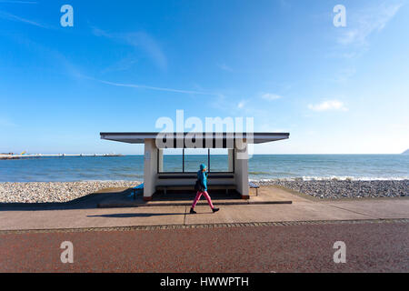 Woman taking an early morning walk along the promenade and in front of a seaside shelter at the popular seaside resort of Llandudno, Wales Stock Photo