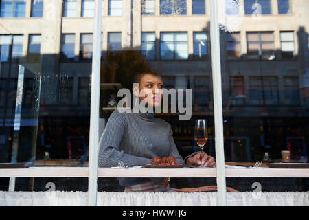 Stylish young woman sitting in cafe seen through window Stock Photo