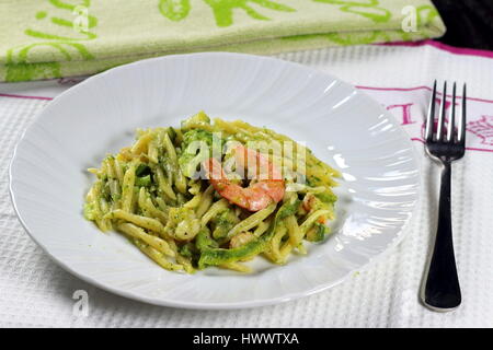 Trofie pasta with prawn (shrimp), broccoli, zucchini (courgette) and tomato in white dish on white kitchen cloth with fork - Italian seafood recipe Stock Photo