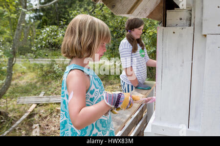 Children painting the exterior of a small playhouse together outside in the garden at summertime Stock Photo