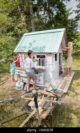 Children painting the exterior of a small playhouse together outside in the garden at summertime Stock Photo