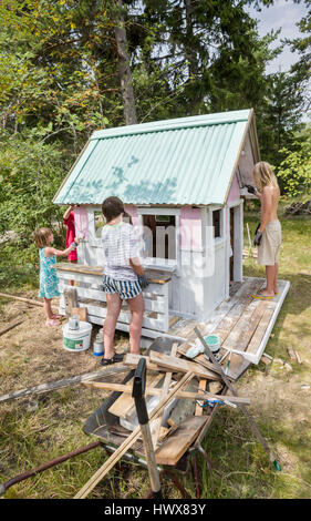 Children painting the exterior of a small playhouse together outside in the garden at summertime Stock Photo