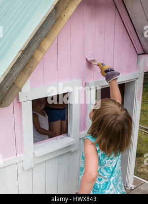 Young girl painting the exterior of a small playhouse Stock Photo