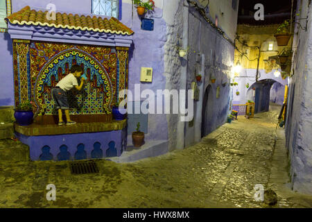 Chefchaouen, Morocco.  Young Boy Drinking at Public Water Tap in the Medina at Night. Stock Photo