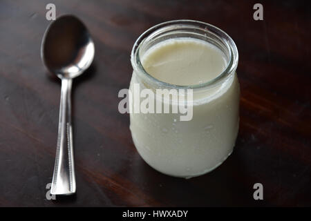 Pot of yogurt on a wooden table with a silver spoon Stock Photo