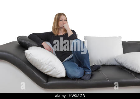 Unhappy ypung woman is sitting on a big black and white couch with black and white pillows. Isolated on the white background. Stock Photo