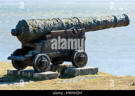 Old, antique cast iron canon pointing out at sea from a defensive wall. Stock Photo