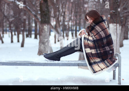 pretty girl with long hair wrapped in a blanket sitting on a ben Stock Photo