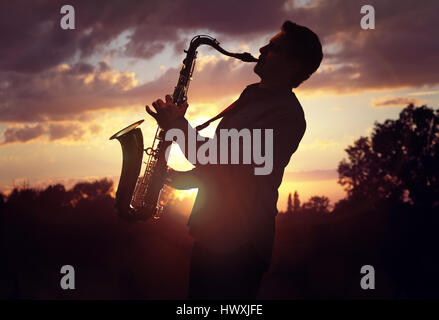 Saxophone player or saxophonist performing sax against sunset Stock Photo