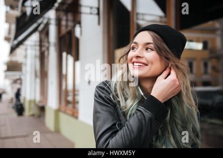 Image of gorgeous young woman wearing hat walking on the street and looking aside. Stock Photo