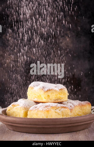 Vertical photo with five portions of traditional homemade cakes filled by sweet curd cheese. Cakes are placed on brown clay plate and covered by powde Stock Photo