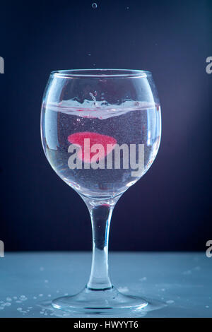 red heart of ice falling with splashes into a glass with a drink a cocktail of heart Stock Photo
