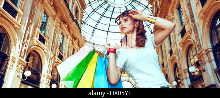 Discover most unexpected trends in Milan. Fashion monger with eyeglasses and colorful shopping bags in Galleria Vittorio Emanuele II looking into the  Stock Photo