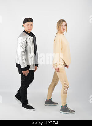 Modern fashionable hipster couple. Young muscular man wearing black clothes, grey jacket and sneakers with girl in yellow clothes on white background Stock Photo