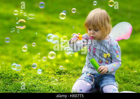 Toddler girl with butterfly wings having fun in the park, blowing soap bubbles Stock Photo