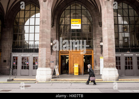 Old woman walking in front of Swiss Post Shop (German: Die Schweizerische Post). Swiss Post is the national postal service of Switzerland. A public co Stock Photo