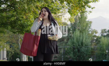 Low angle view of happy woman walking and eating groceries Stock Photo