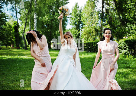 Bride posed on park with two cute brunette bridesmaids on pink dresses. Stock Photo