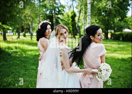 Bride posed on park with two cute brunette bridesmaids on pink dresses. Stock Photo