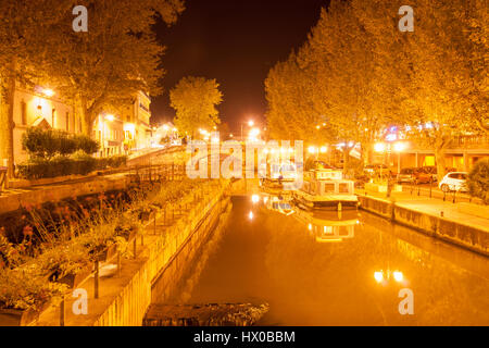 Canal boats moored alongside on Canal de la Robine at night under golden light Narbonne, France. Stock Photo